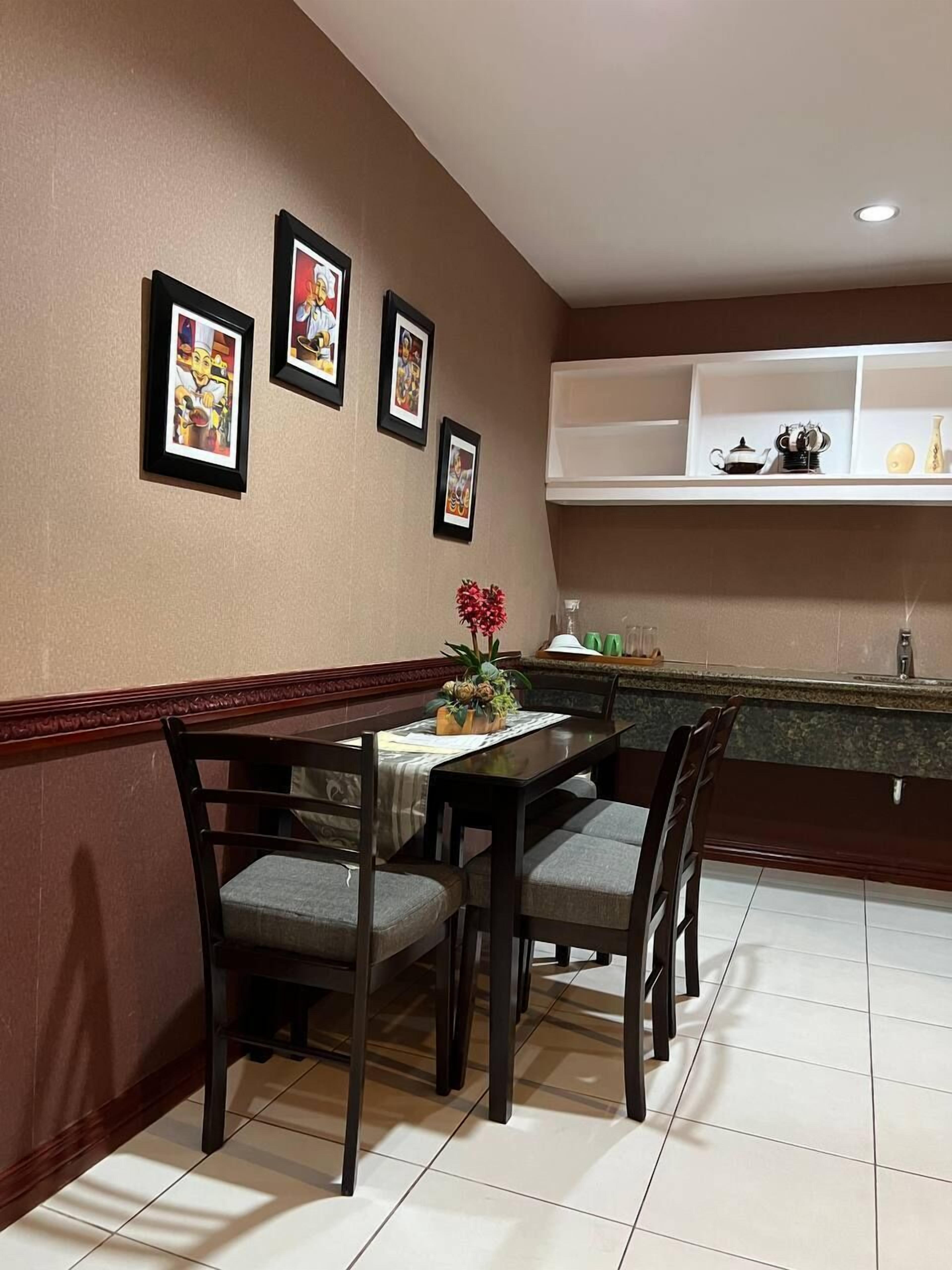 Un comedor con una mesa dispuesta para cuatro personas, rodeada de sillas. Hay cuadros enmarcados en la pared sobre la mesa.