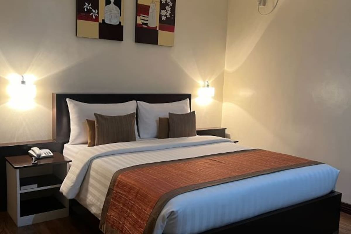 A hotel room with a large bed, two bedside tables, a nightstand, and two wall-mounted lamps.