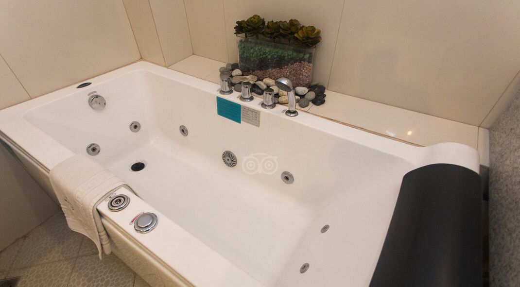 A modern bathroom with a white bathtub, multiple faucets, and a small plant on the side.