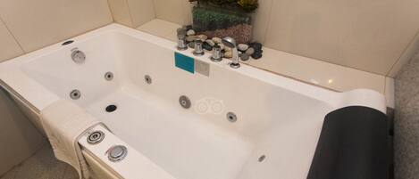 Un baño moderno con una bañera blanca, múltiples grifos y una pequeña planta a un lado.