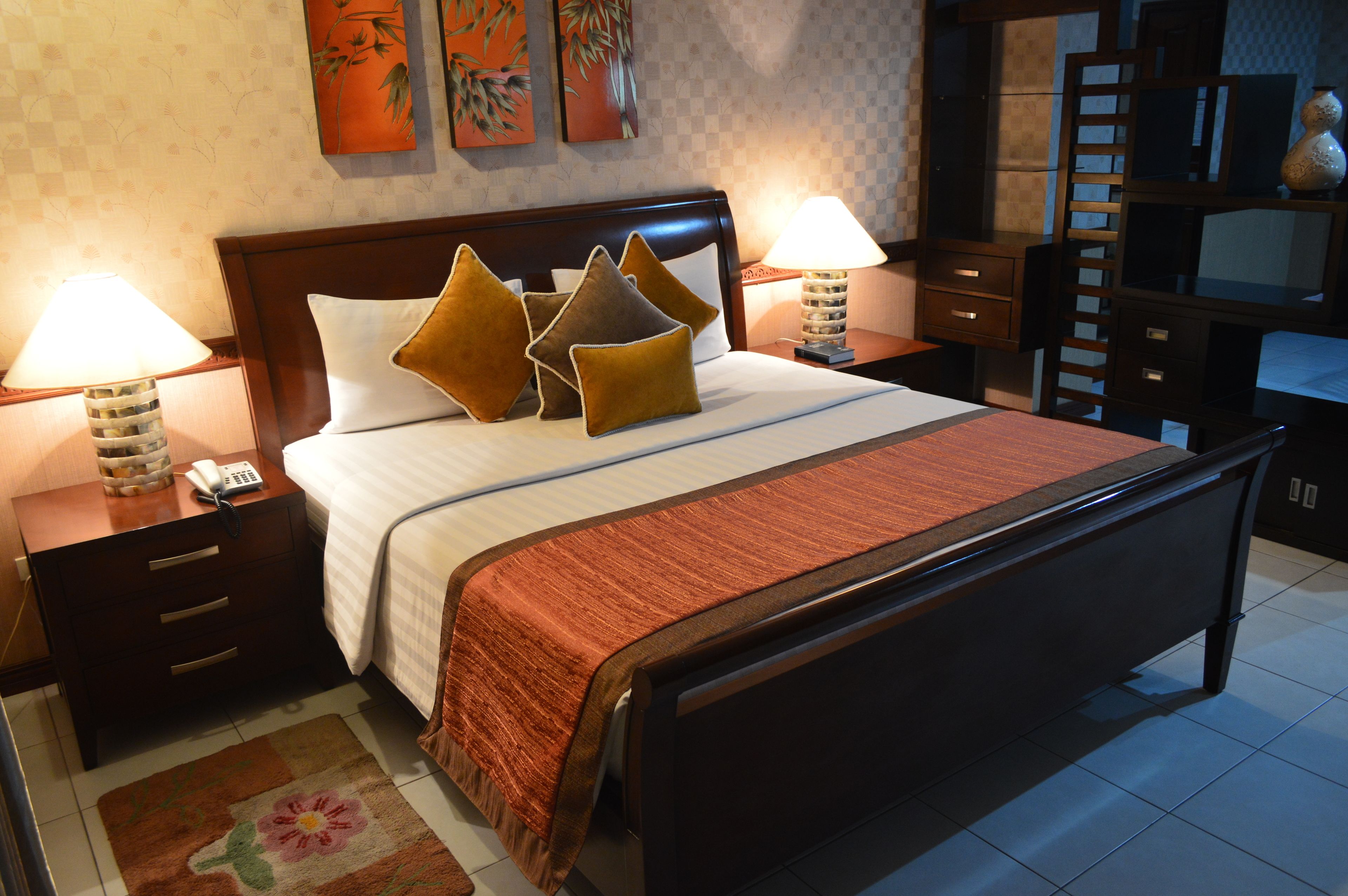 A neatly made bed with a wooden headboard, two bedside lamps, and a floral area rug.