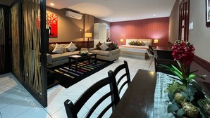 Una sala moderna con un sofá, una mesa de centro y una mesa de comedor con sillas. Hay una pared de ladrillo rojo decorativa y una planta ornamental sobre la mesa del comedor.