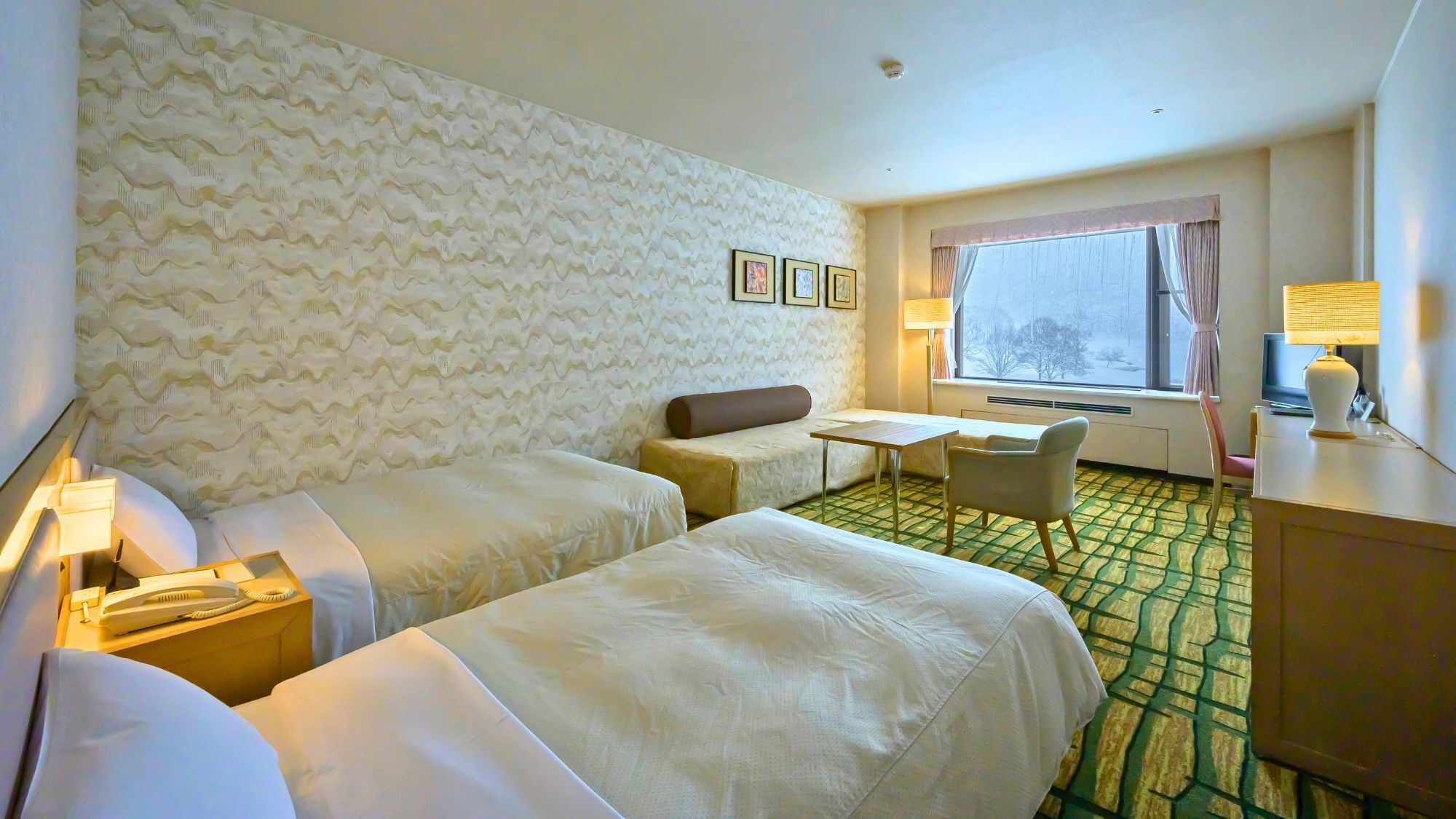 A hotel room with two beds, a small table, a sofa, a TV, a lamp, and a window with a view.