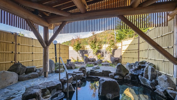 A traditional Japanese onsen with a wooden structure, stone steps, and a rock-lined pool. - Hotel Tangram (Shinano)