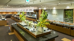 A modern hotel kitchen with a buffet setup, featuring a central counter with floral arrangements and a variety of dishes. - Hotel Tangram (Shinano)