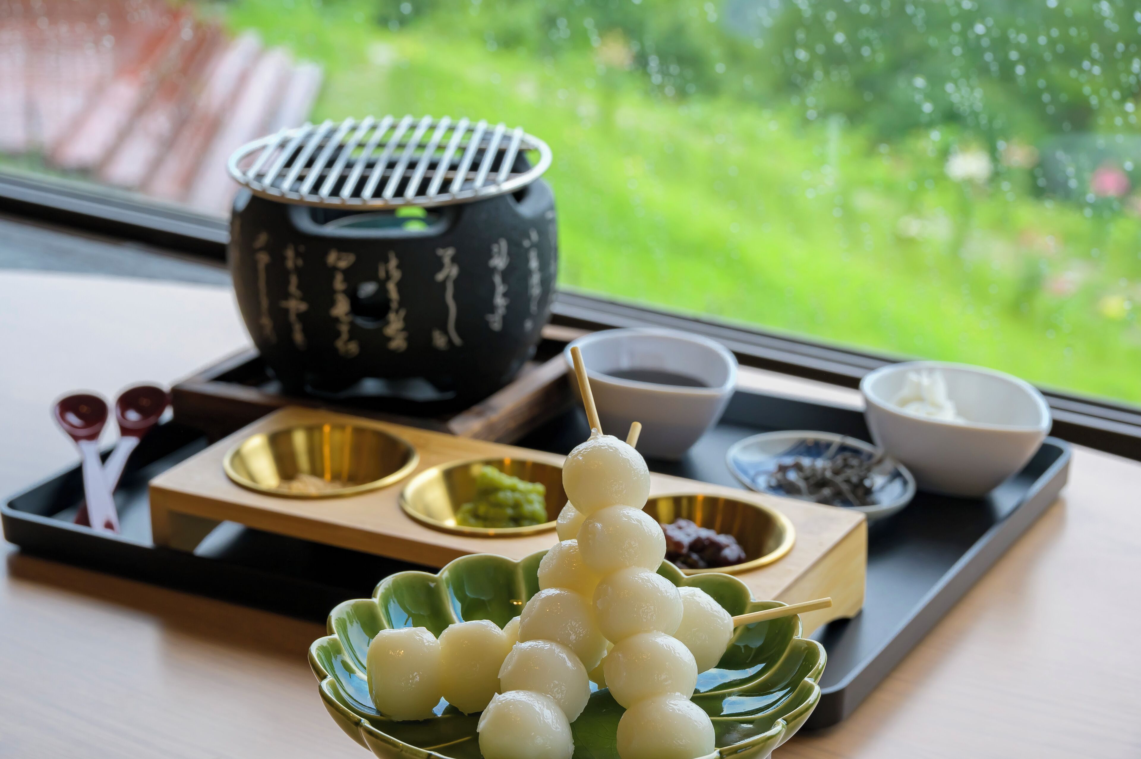 A tray with a bowl of white spherical food items, a bowl of green food, and a black pot with gold patterns.