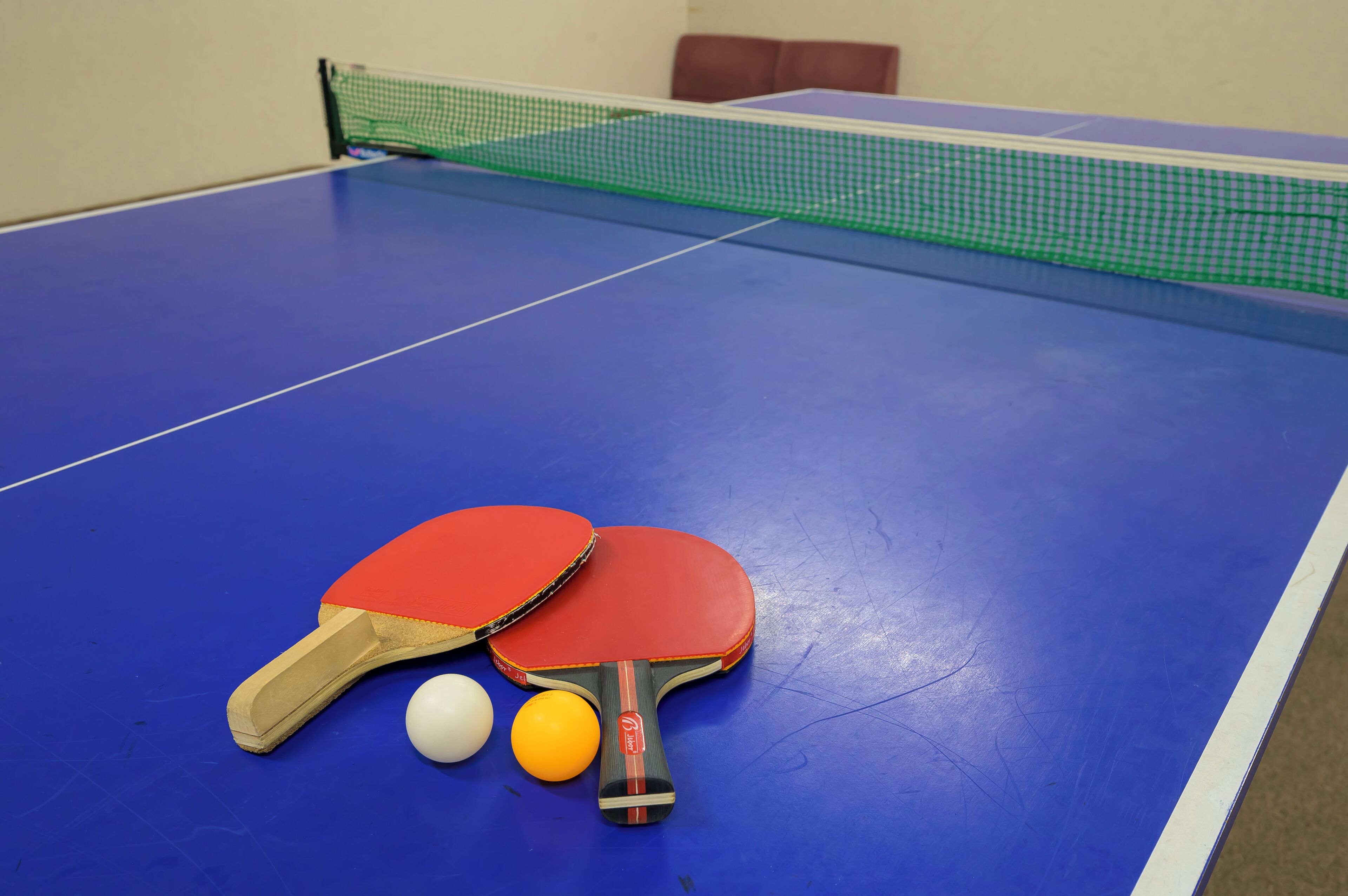A blue ping pong table with two red paddles and two balls.