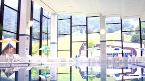 A large indoor swimming pool with clear glass walls, multiple lounge chairs, and umbrellas. - Hotel Tangram (Shinano)