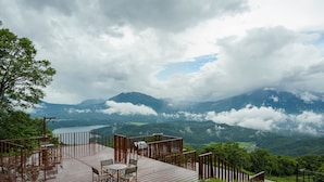 A wooden deck with outdoor seating and a scenic view of mountains and a lake. - Hotel Tangram (Shinano)