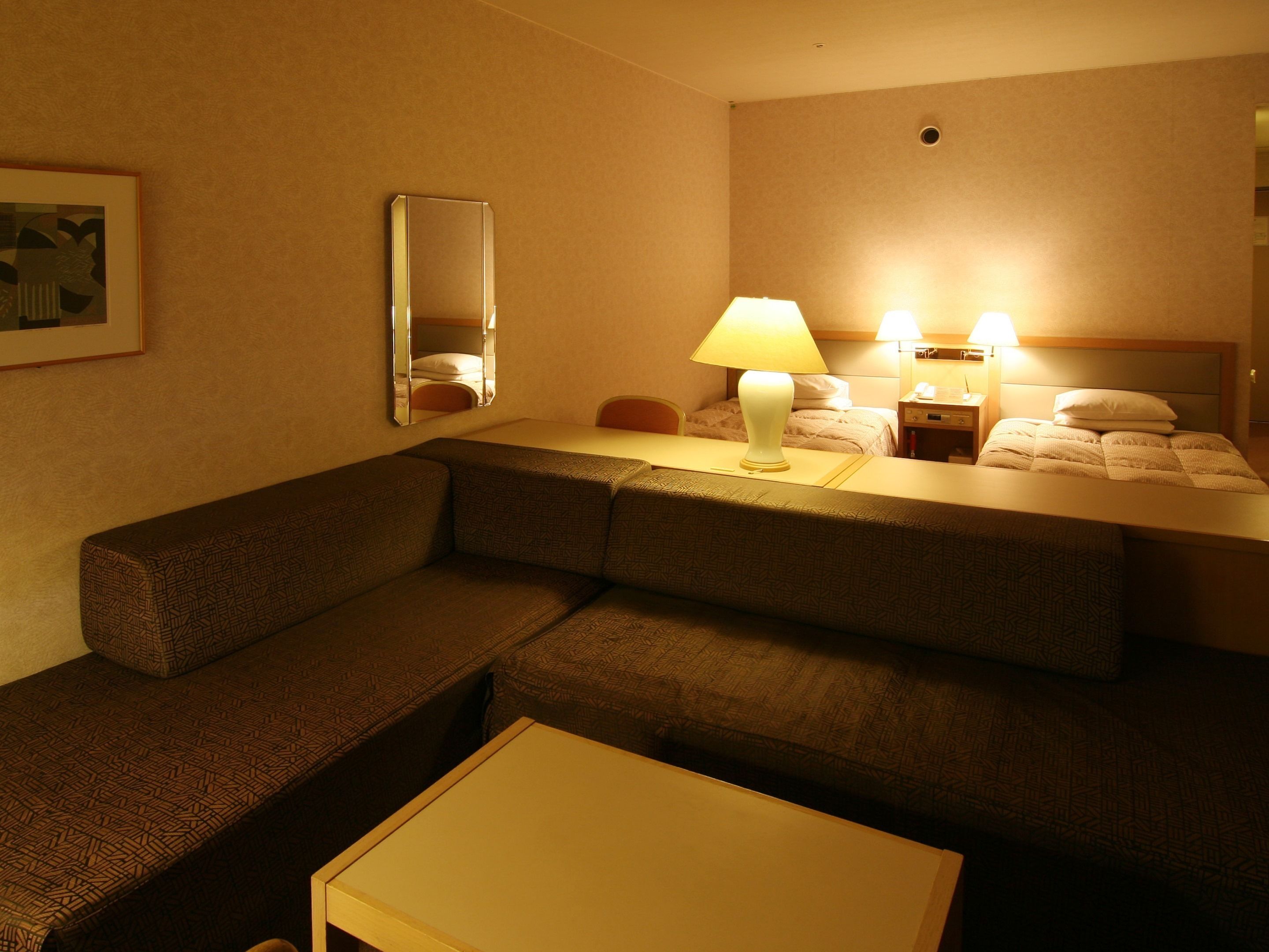 Habitación de hotel con sofá, una mesita, cama con cabecera, mesita de noche, lámpara y espejo.