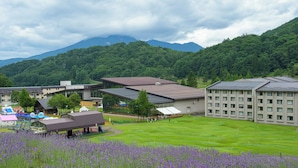 A hotel with multiple buildings, a golf course, and a mountain backdrop. - Hotel Tangram (Shinano)
