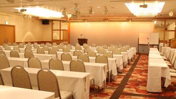 Un salón de conferencias con filas de mesas y sillas, un atril y una pizarra.
