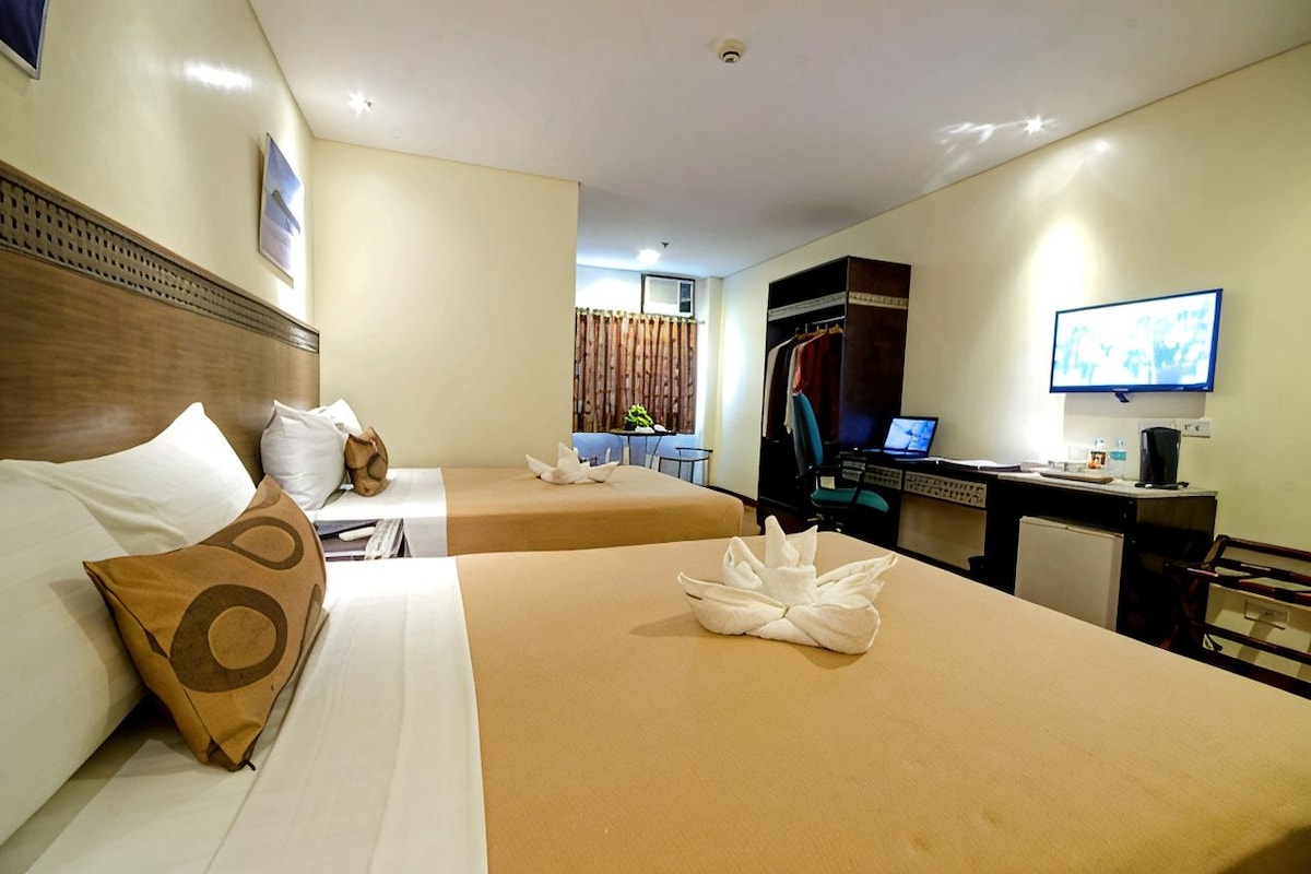 Ein Hotelzimmer mit zwei Betten, einem Schreibtisch mit Computer, einem Fernseher und einem Kleiderschrank.