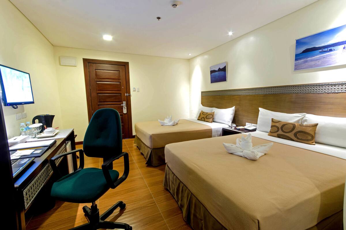 Ein Hotelzimmer mit zwei Betten, einem Schreibtisch mit Computer, einem Stuhl und einer Tür.