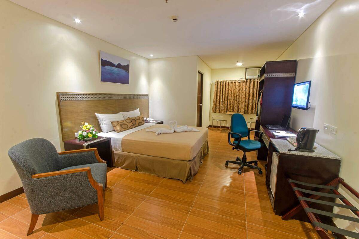 Ein Hotelzimmer mit Bett, Schreibtisch, Stuhl, Fernseher und einem Bild an der Wand.
