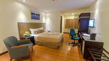 A hotel room with a bed, a desk, a chair, a TV, and a painting on the wall.
