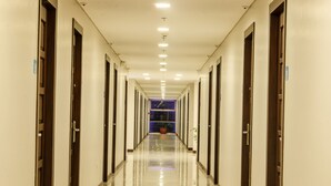 A long, well-lit hallway with doors on both sides, leading to a room with a blue-lit window and a potted plant. - Fersal Hotel Puerto Princesa (Puerto Princesa)