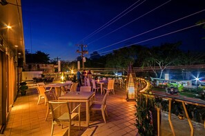 Un espace extérieur aménagé en terrasse, avec des tables et des chaises, donnant sur la rue, et décoré d’un sapin de Noël.