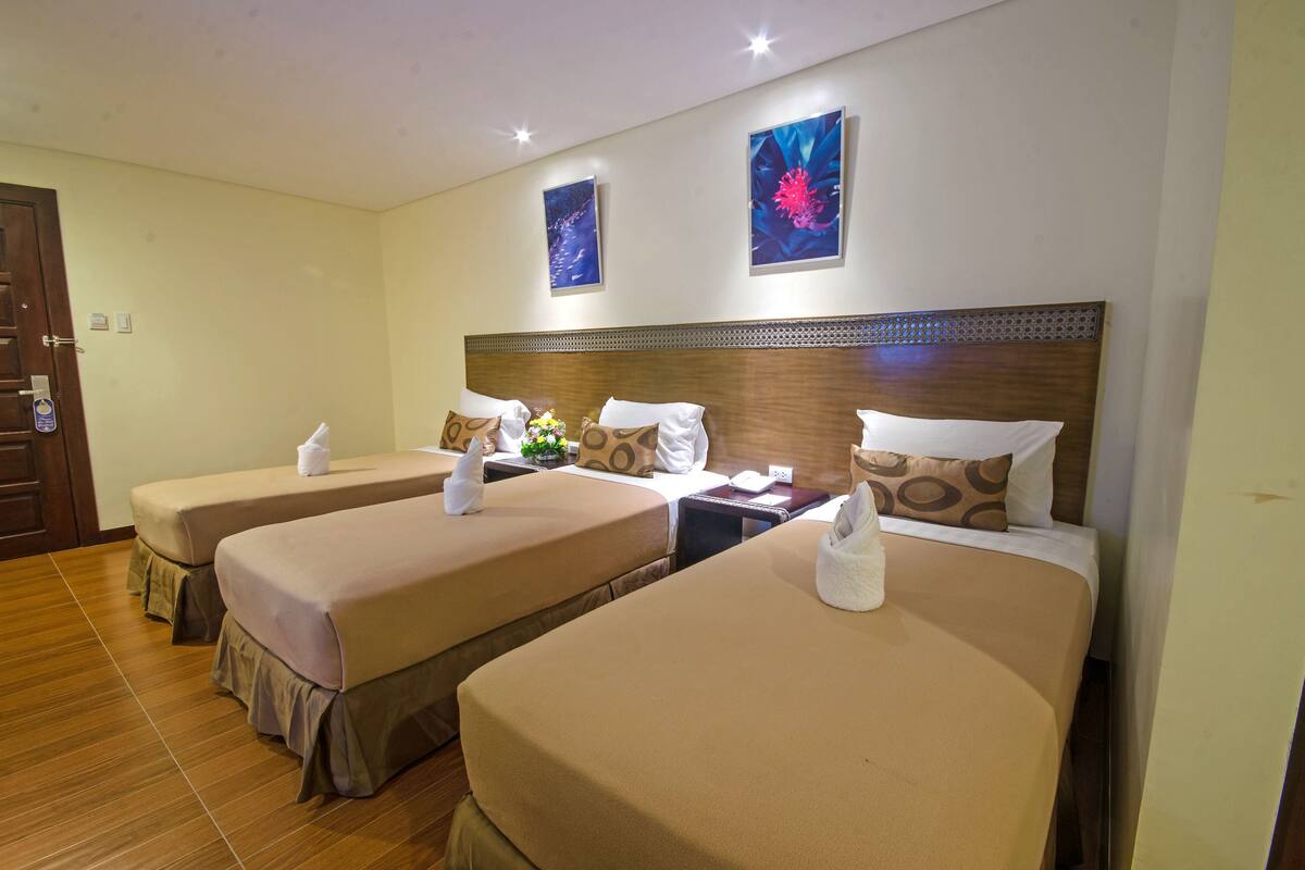 Ein Hotelzimmer mit zwei Einzelbetten, jeweils mit beiger Bettdecke und passenden Kissen. Zwei Nachttische mit Lampen, ein hölzernes Kopfteil und ein Kunstwerk an der Wand sind ebenfalls vorhanden.