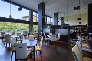 Un restaurante espacioso con techos altos, amplias ventanas y vistas al exterior con vegetación. Mesas y sillas dispuestas para comer.