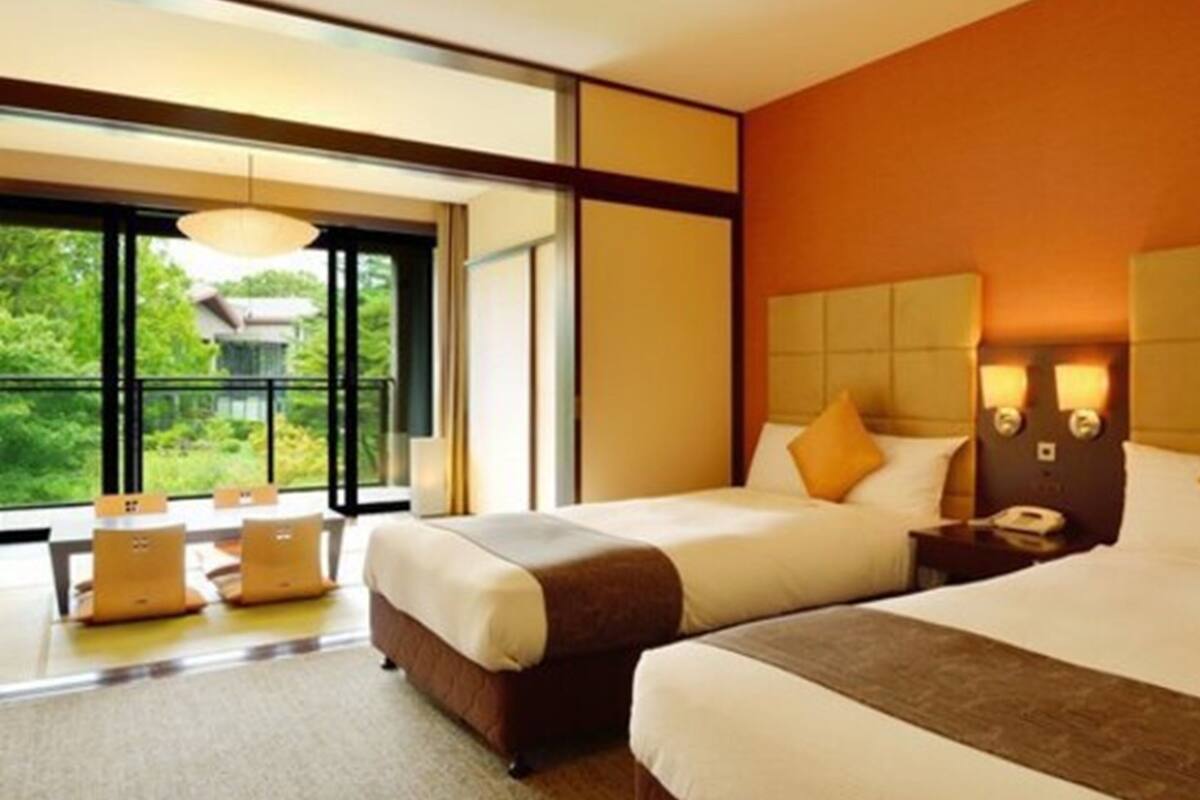 A modern hotel room with two beds, a large window, and a seating area with a table and chairs.