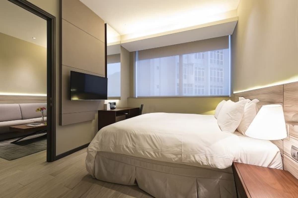 Een moderne hotelkamer met een groot bed, een bureau, een flatscreen televisie aan de muur en een raam met uitzicht op gebouwen.