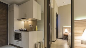 Una cocina moderna con electrodomésticos integrados, un pequeño comedor y un dormitorio independiente con mesita de noche y lámpara.