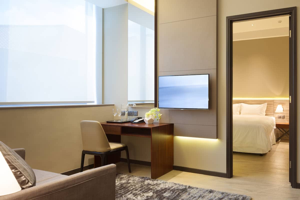 Habitación de hotel con escritorio, silla, cama, televisor y vistas al exterior.
