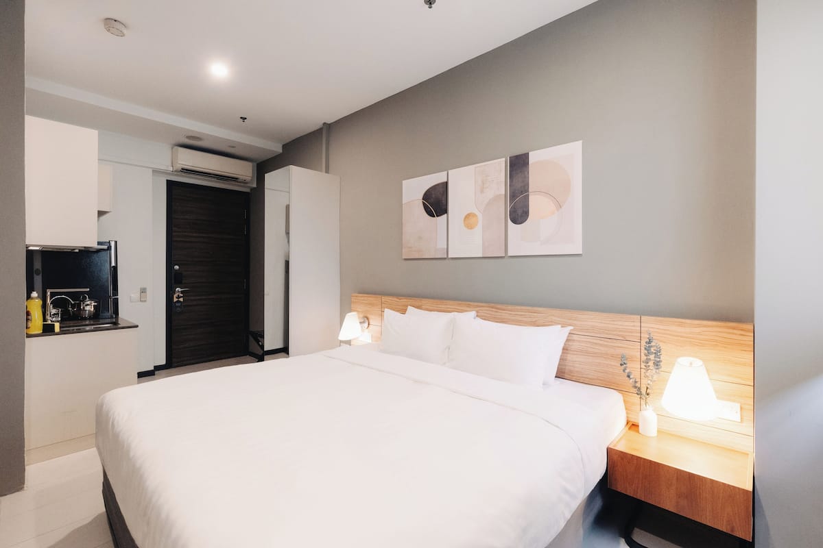 Una habitación de hotel moderna con una cama grande, lámparas de noche, una mesita con un florero y arte abstracto en la pared.