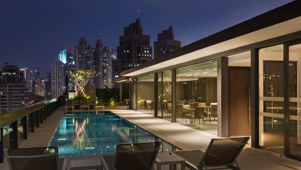 Una piscina en la azotea con sillones, vista al horizonte urbano y arquitectura moderna.