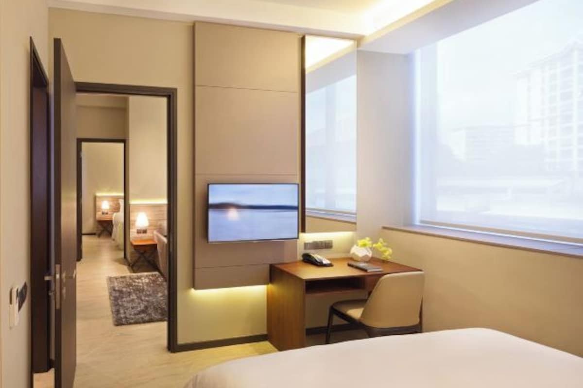 Een hotelkamer met een bed, een bureau met stoel, een aan de muur bevestigde televisie en een raam met uitzicht.