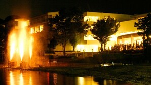 Una vista nocturna de un edificio con una fuente y una superficie acuática reflectante.