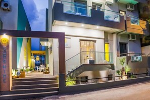 A modern hotel with a glass entrance, outdoor seating, and a staircase leading to the upper floors. - Sunshine Hotel (Malia)