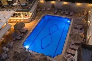 A rooftop swimming pool with lounge chairs and umbrellas, surrounded by a bar area. - Sunshine Hotel (Malia)