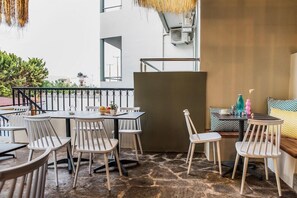 An outdoor seating area with tables and chairs, a stone floor, and a view of buildings in the background. - Sunshine Hotel (Malia)