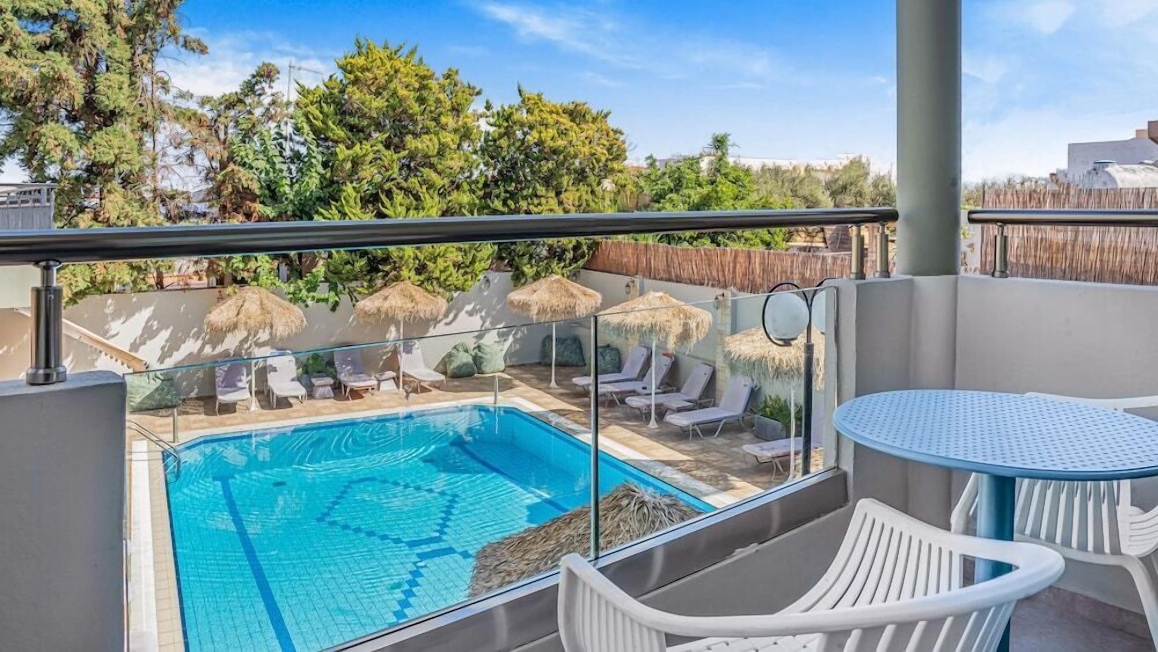 A rooftop pool area with lounge chairs and a table, surrounded by a wooden fence and trees.