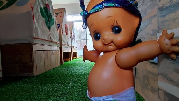 A doll on artificial grass in a room with wooden walls and a cactus-themed decoration. - Pon Pon Woo (Kaohsiung)
