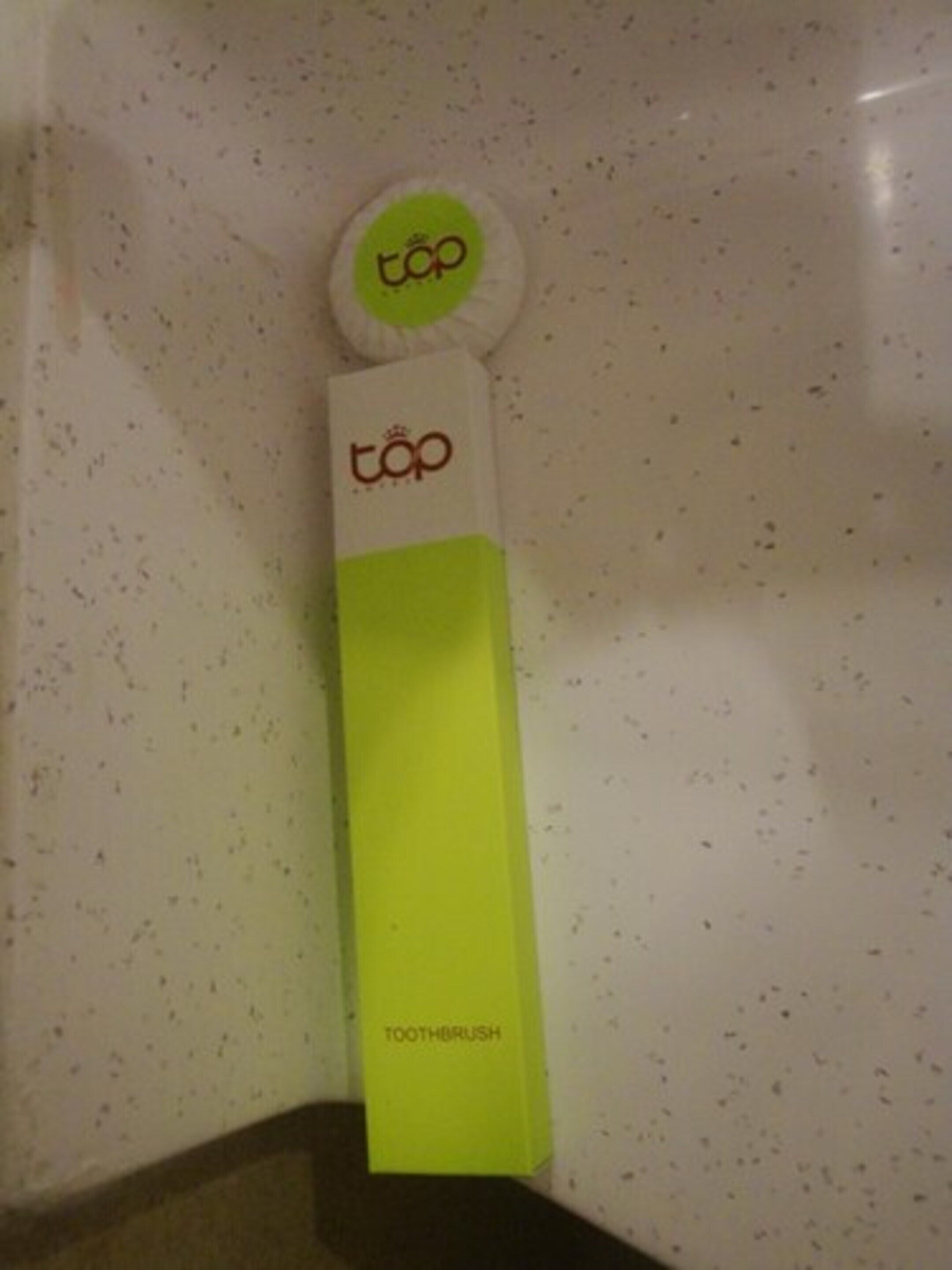 A toothbrush holder with the brand 'top' on a white speckled wall.