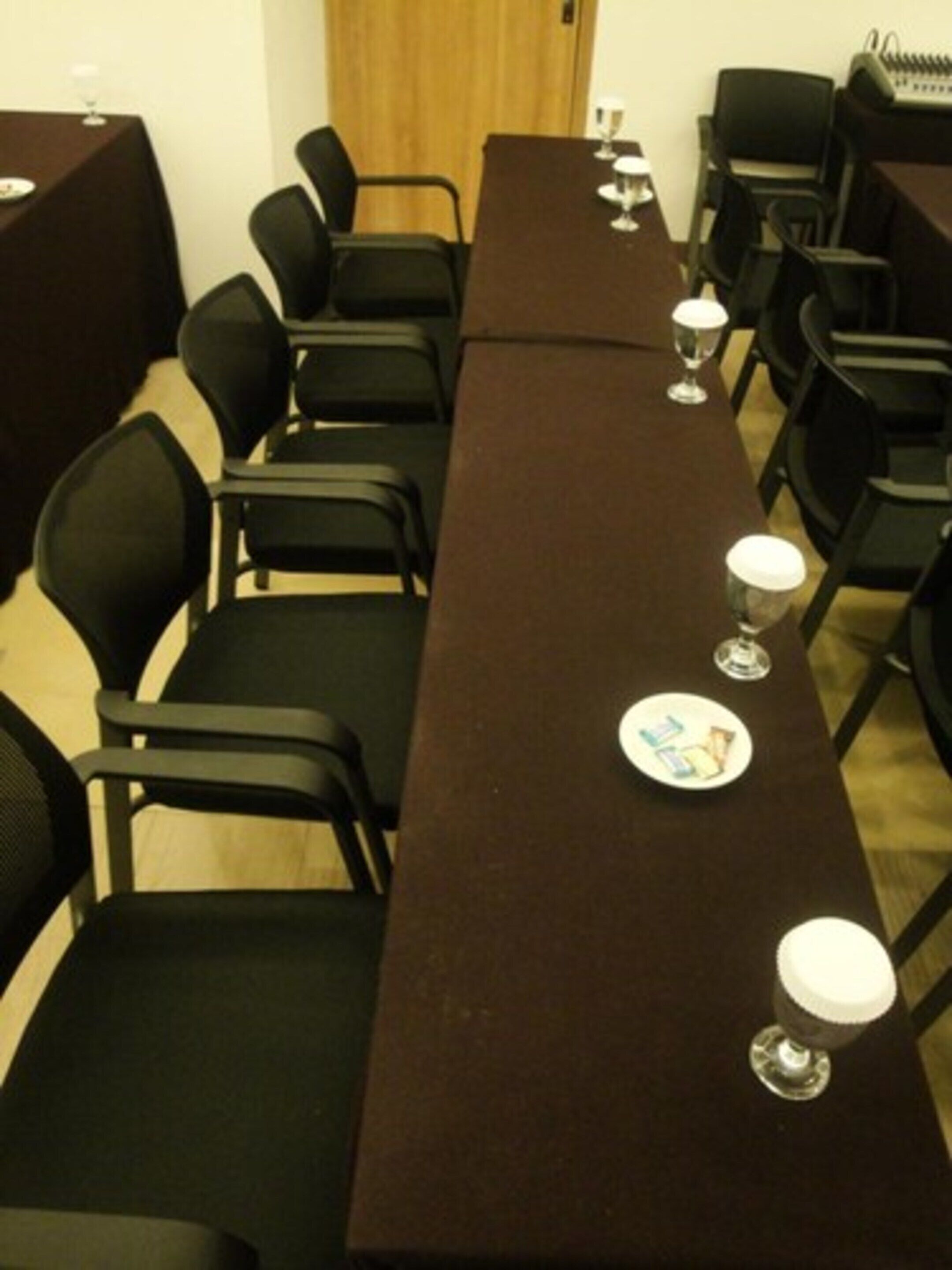 Een vergaderzaal met een lange tafel, zwarte stoelen en enkele wijnglazen en borden op de tafel.