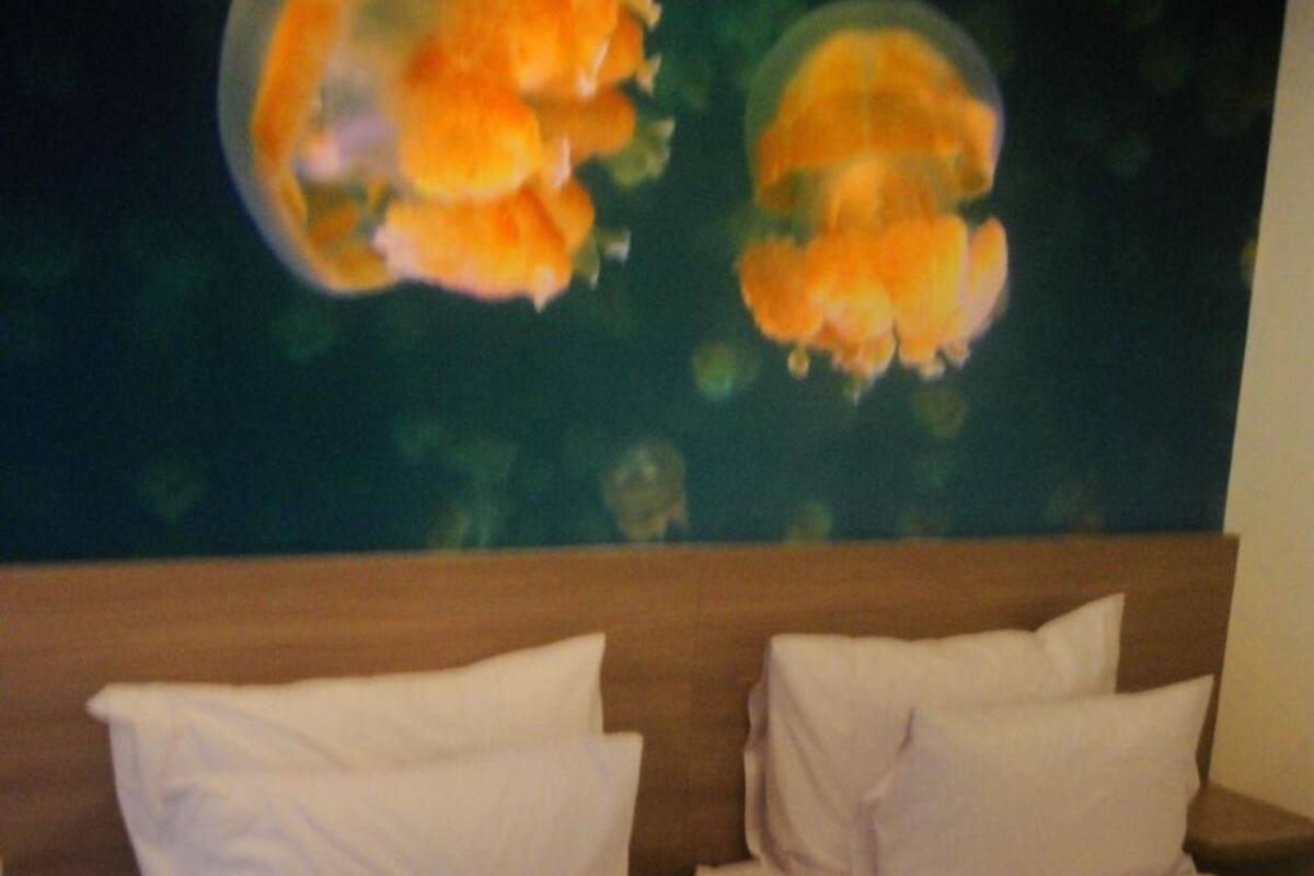 Une chambre d’hôtel avec deux lits, une tête de lit en bois et un tableau représentant des méduses accroché au mur.