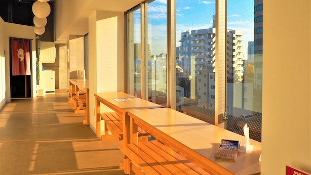Un hall d’hôtel moderne, doté de bancs en bois, de grandes fenêtres offrant une vue sur la ville et d’un design épuré et minimaliste.