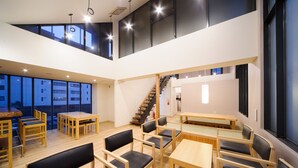 Un espace de restauration spacieux et bien éclairé, avec plusieurs tables et chaises, un escalier et de grandes fenêtres donnant sur l’extérieur.