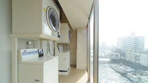 Une buanderie équipée de machines à laver et de sèche-linge, d’un distributeur d’eau et offrant une vue sur une rivière où naviguent des bateaux.