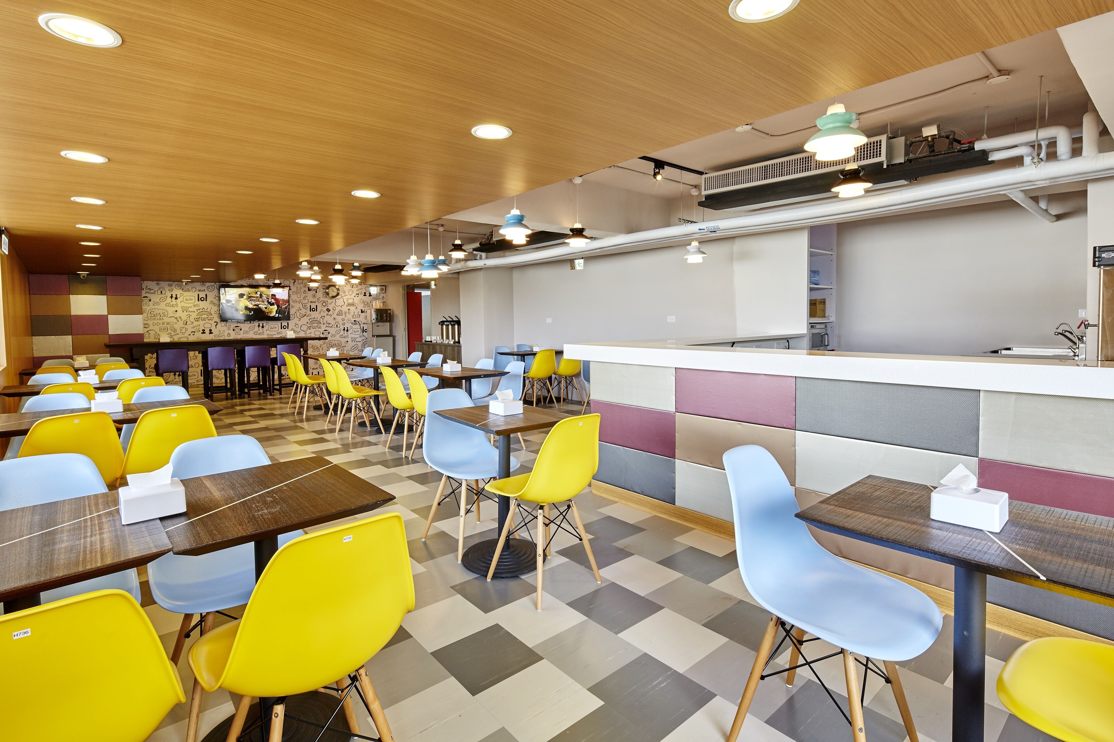 Un restaurante moderno con sillas amarillas y azules, mesas de madera y una recepción.
