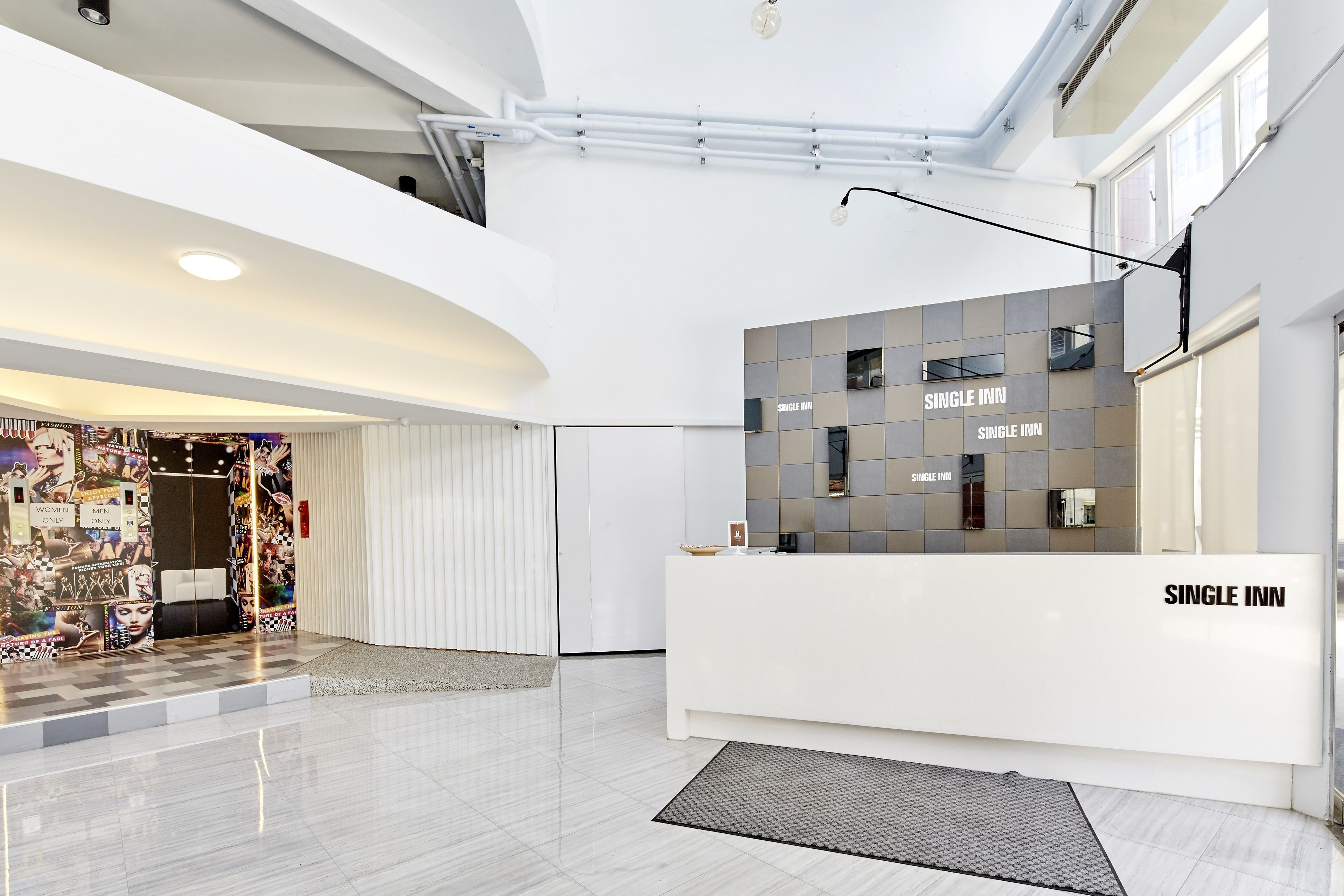 A modern hotel lobby with a reception desk labeled "SINGLE INN" and a check-in counter.
