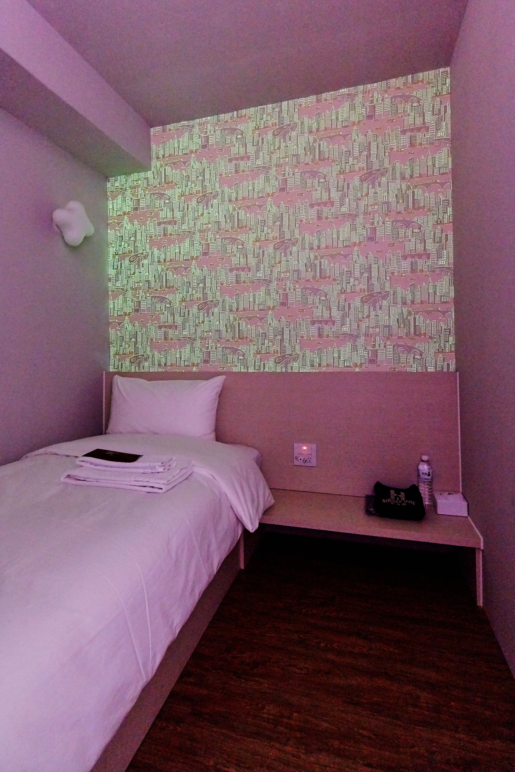 A bedroom with a bed, a nightstand, a wall-mounted projector, and a patterned wall.