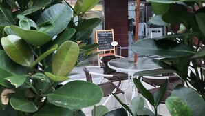 A patio area with round tables and chairs, surrounded by lush green plants. A chalkboard menu is visible, and the entrance to a building is seen in the background. - Single Inn Taipei - Hostel (New Taipei City)