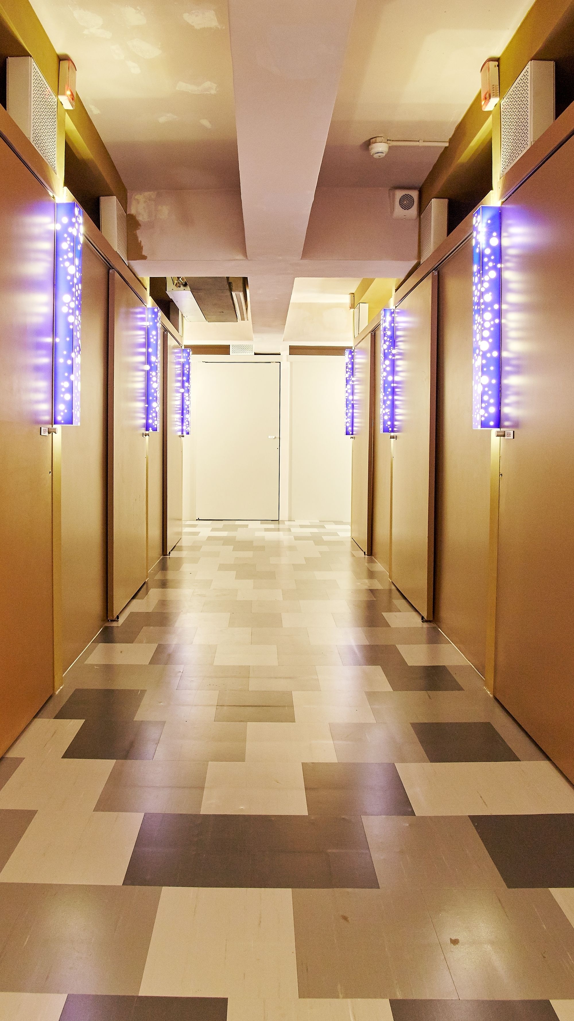 A hotel hallway with check-in counters, a tiled floor, and a ceiling with recessed lighting.