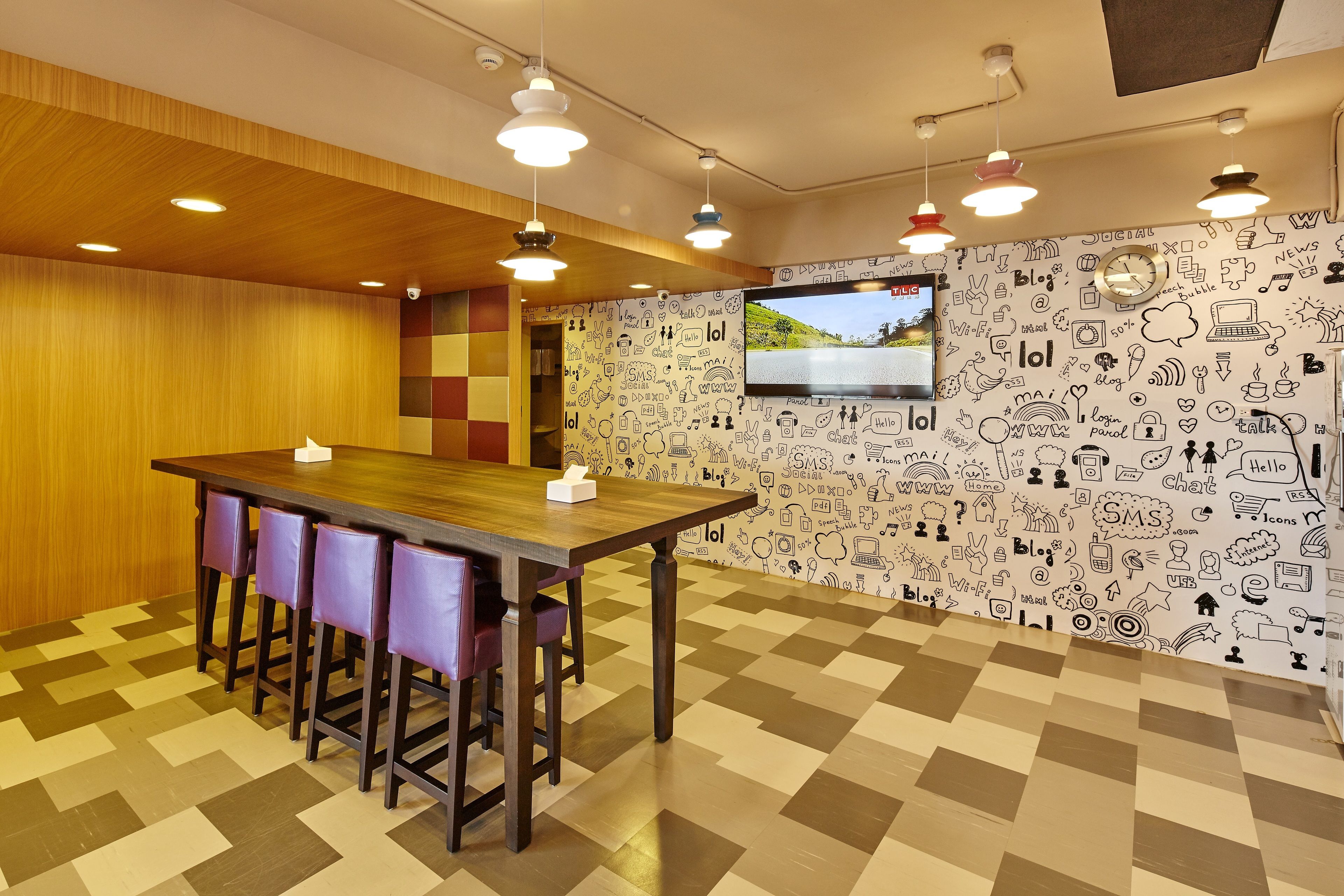 A conference room with a wooden table, purple chairs, a large screen, and a patterned wall.