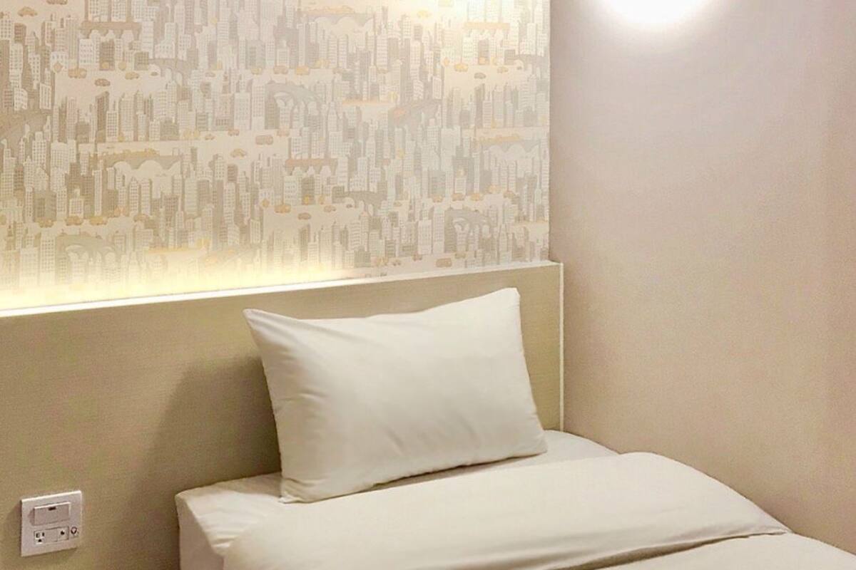 A neatly made bed with white bedding and a pillow, a bedside table, and a wall with a cityscape wallpaper.